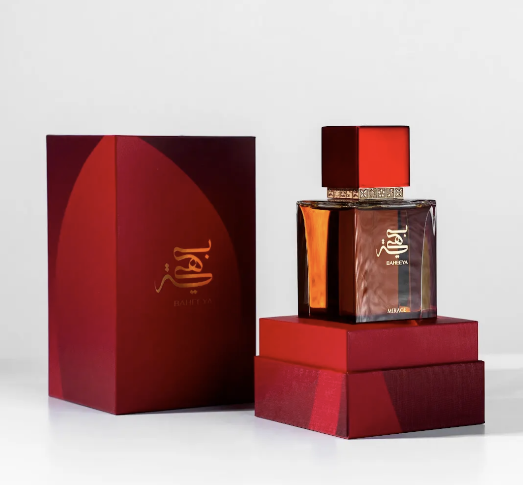 A luxury perfume bottle with a square amber-brown glass body and a glossy red cap, displayed next to its matching deep red presentation box on a clean white background.